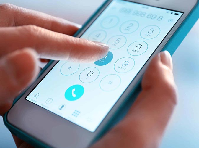 ​Mężczyzna  siedzący przy biurku i trzymający telefon w dłoni, gdzie na ekranie telefonu widać wskaźnik rozładowanej baterii.