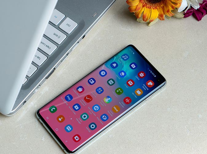​Mężczyzna  siedzący przy biurku i trzymający telefon w dłoni, gdzie na ekranie telefonu widać wskaźnik rozładowanej baterii.
