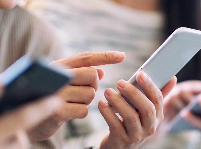 ​Mężczyzna  siedzący przy biurku i trzymający telefon w dłoni, gdzie na ekranie telefonu widać wskaźnik rozładowanej baterii.