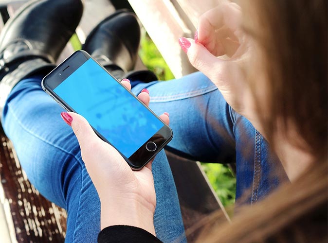 ​Mężczyzna  siedzący przy biurku i trzymający telefon w dłoni, gdzie na ekranie telefonu widać wskaźnik rozładowanej baterii.
