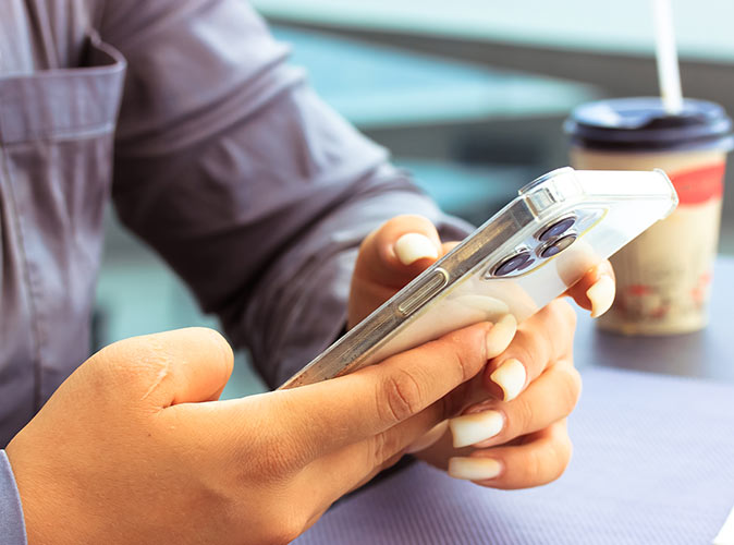 ​Mężczyzna  siedzący przy biurku i trzymający telefon w dłoni, gdzie na ekranie telefonu widać wskaźnik rozładowanej baterii.